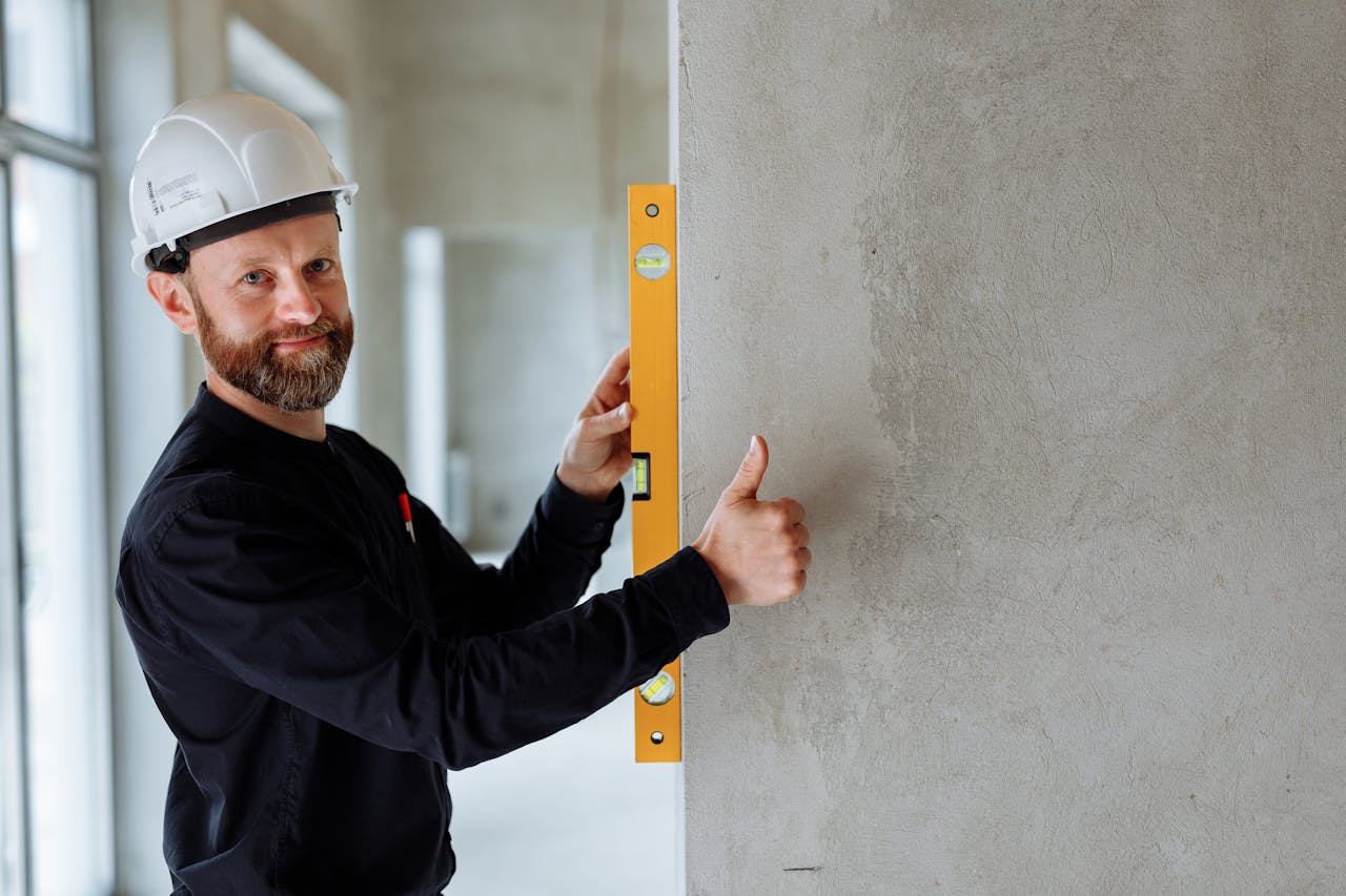 Confident male construction worker using a spirit level on a concrete wall for precise alignment indoors.